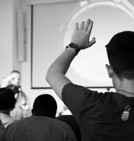 A man holding up a hand to ask a question at a presentation.